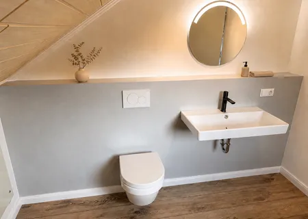 Zweites Bad der Ferienwohnung Am Wäldchen unter der Dachschräge mit Wand-WC, Waschtisch und rundem LED-Spiegel